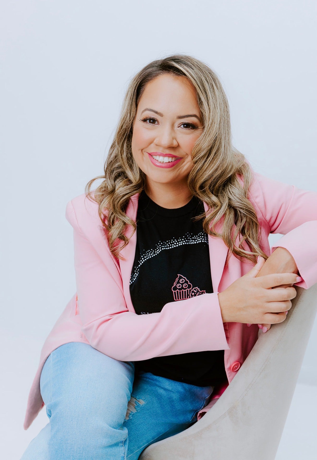 Woman wearing a pink jacket and black shirt with a graphic design, sitting on a white surface.